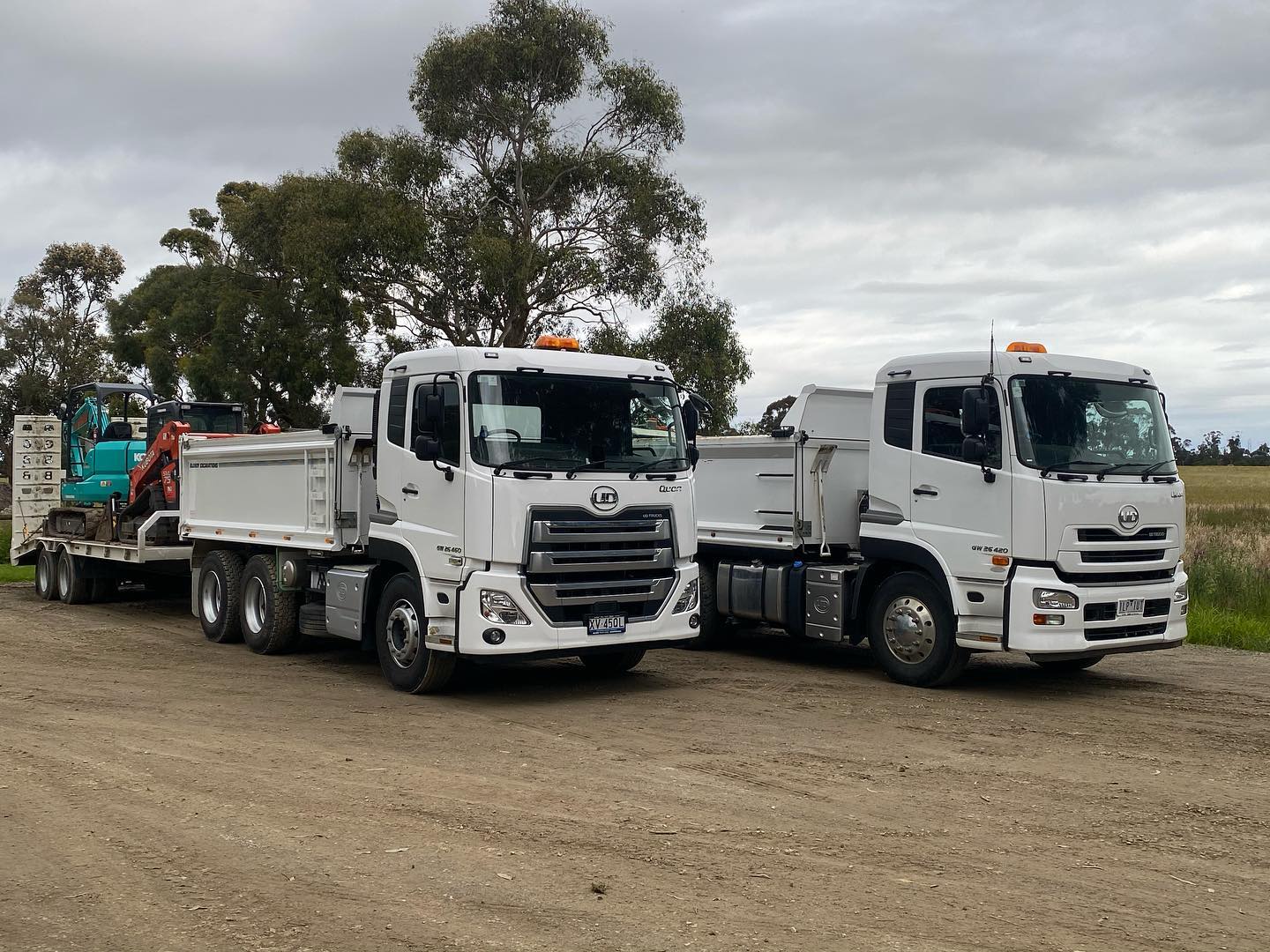 Two white trucks and excavators on a dirt road.