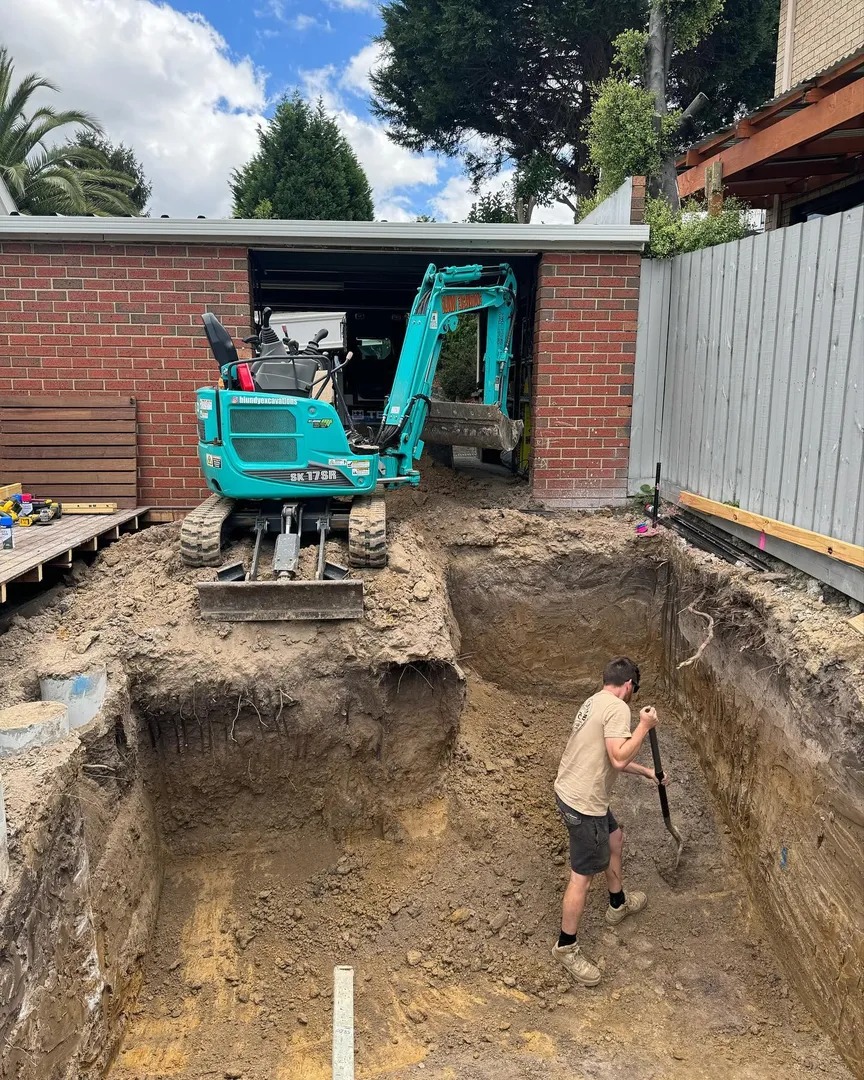 Excavator digging a large hole near garage
