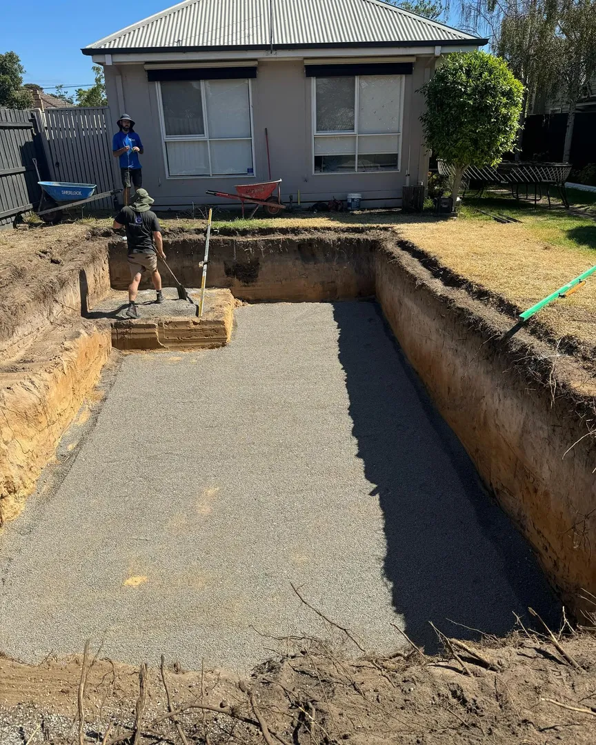 Two workers digging pool foundation near house