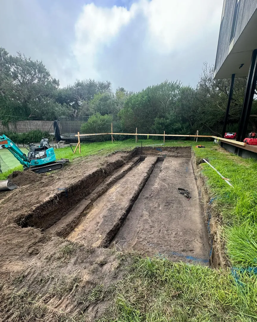 Backyard excavation site with small blue excavator